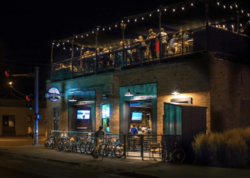 A lively restaurant at night with outdoor seating, string lights, and bicycles parked outside.