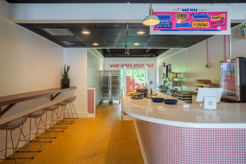 Bright, modern café interior with a counter, bar seating, and a colorful menu sign on the wall.