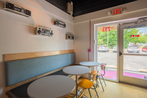 A cozy cafe interior with round tables, wooden chairs, and vintage boomboxes on the wall, near a glass door.