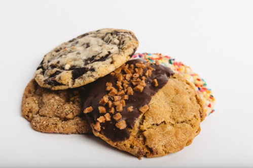 A stack of three cookies: one with chocolate chunks, one with toffee bits, and one with colorful sprinkles.