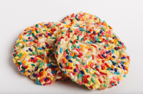 Three colorful cookies covered in vibrant sprinkles, arranged on a white surface.