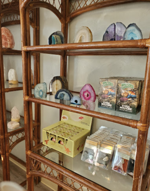 A wooden shelf displaying various crystals, geodes, and collectible card packs in a cozy shop setting.