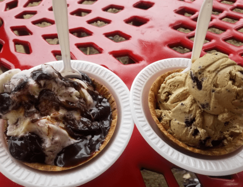 Two ice cream sundaes in paper bowls on a red table. One has chocolate sauce, the other is cookies and cream.