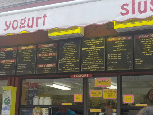 Menu board displaying various yogurt, sundae, and slush flavors, including cones, soft serve, and specialty items.