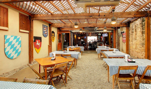 Cozy restaurant interior with wooden tables, checkered tablecloths, and decorative shields on the walls.