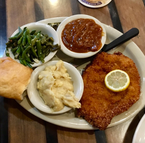 A plate featuring fried fish with lemon, mashed potatoes, green beans, baked beans, and a roll.