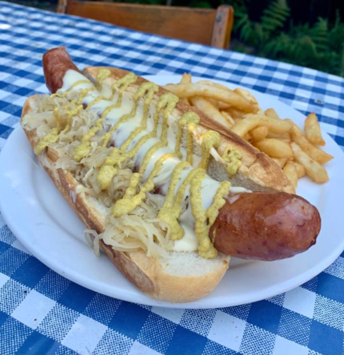 A large hot dog topped with sauerkraut and mustard, served on a bun with a side of French fries on a checkered tablecloth.
