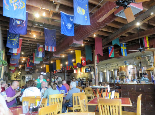 A lively restaurant interior with wooden tables, patrons dining, and colorful flags hanging from the ceiling.