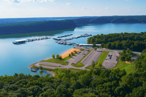Aerial view of a serene lake with a marina, parking area, and lush green trees surrounding the water.
