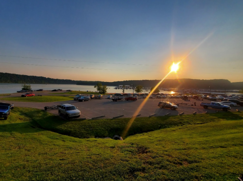 Sunset over a lake with parked cars and grassy areas, creating a serene outdoor scene.