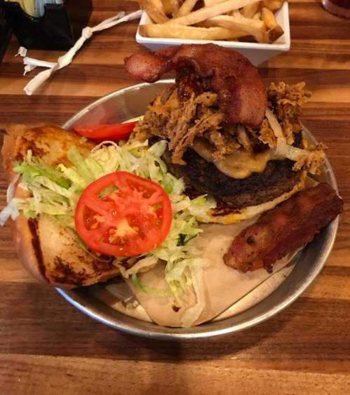 A hearty burger topped with pulled pork, bacon, lettuce, and tomato, served with a side of fries.