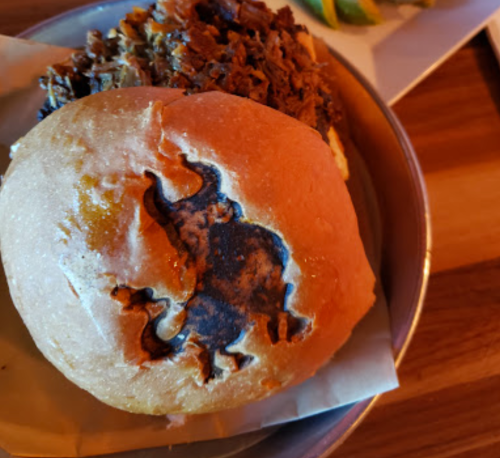A close-up of a bun with a dark imprint of a buffalo, topped with shredded meat on a plate.