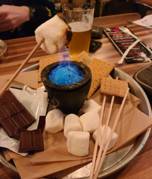 A tray with a small pot of blue flame, graham crackers, chocolate, marshmallows, and a toasted marshmallow on a stick.
