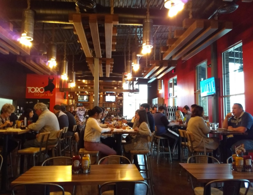 A bustling restaurant interior with patrons dining at tables, warm lighting, and a vibrant red wall.