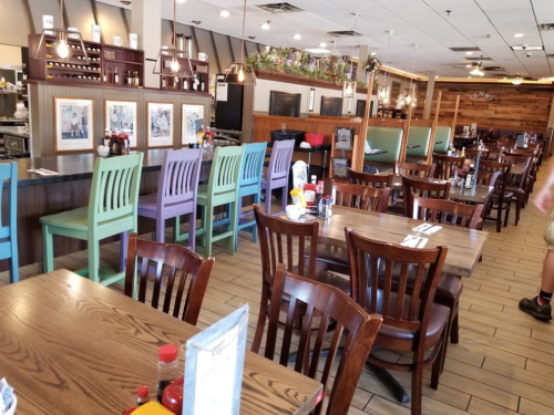 A spacious restaurant interior with wooden tables, colorful chairs, and condiment bottles on the tables.