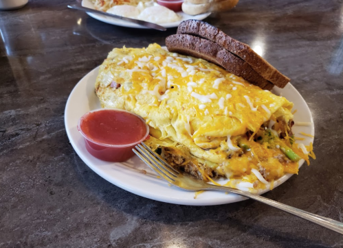 A plate of cheesy omelette with vegetables, served with toast and a side of red sauce.