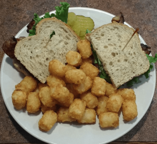 A plate with a sandwich made of lettuce and bacon, served with a side of crispy tater tots and pickles.