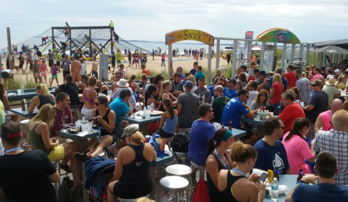 A crowded beachside restaurant with people dining and enjoying activities in the background, including a climbing structure.