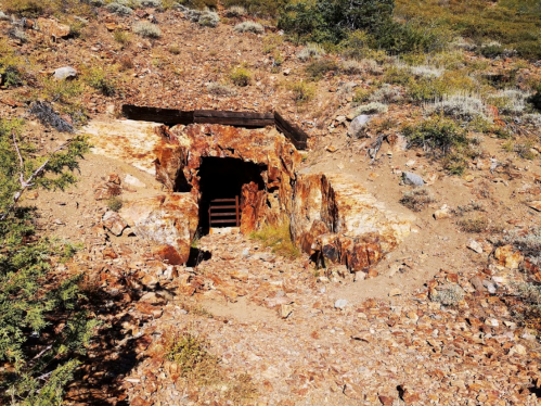 Abandoned mine entrance surrounded by rocky terrain and sparse vegetation.