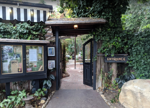 A garden entrance framed by greenery, featuring a sign that reads "ENTRANCE" and a pathway leading into the garden.