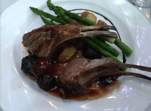 A plate featuring two lamb chops, asparagus, roasted potatoes, and a berry sauce.