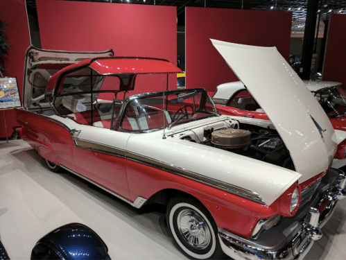 A classic red and white convertible car displayed in a museum, with the hood open showcasing the engine.