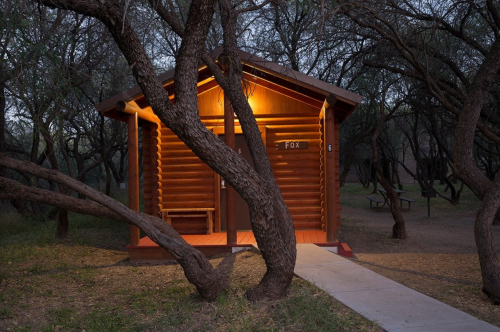 A cozy log cabin illuminated at night, surrounded by trees and a pathway leading to the entrance.
