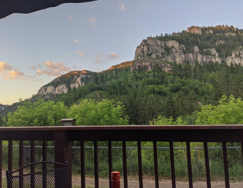 A scenic view of mountains and lush greenery at sunset, seen from a wooden deck.