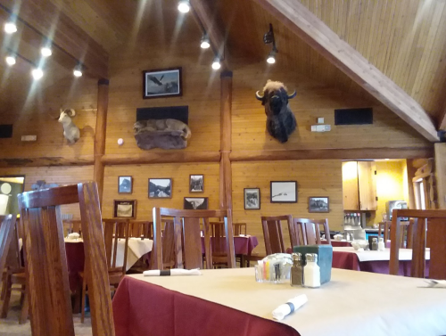 Interior of a rustic restaurant with wooden beams, mounted animal heads, and tables set with red tablecloths.