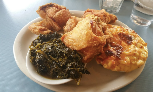 A plate of fried chicken, macaroni and cheese, and collard greens served on a white dish.