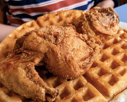 A close-up of crispy fried chicken pieces served on a golden waffle.