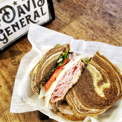 A close-up of a sandwich with layers of turkey, cheese, lettuce, and tomato on marbled rye bread, placed on parchment paper.