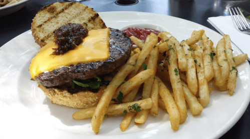 A cheeseburger with melted cheese and a topping, served with crispy fries and a side of ketchup on a white plate.