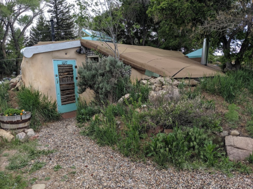 A unique earth-sheltered home with a sloped roof, surrounded by greenery and a gravel path leading to the entrance.