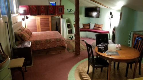 Cozy, rustic room with a bed, dining table, and seating area, featuring green walls and warm lighting.