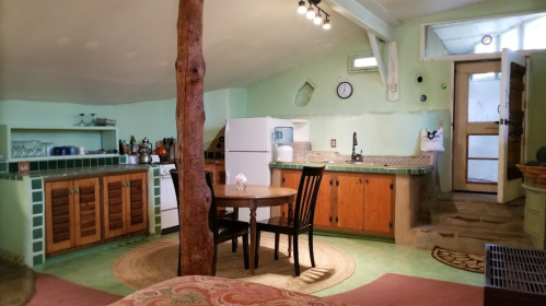Cozy kitchen with green walls, wooden cabinets, a round table, and a rustic tree pillar in a bright, inviting space.