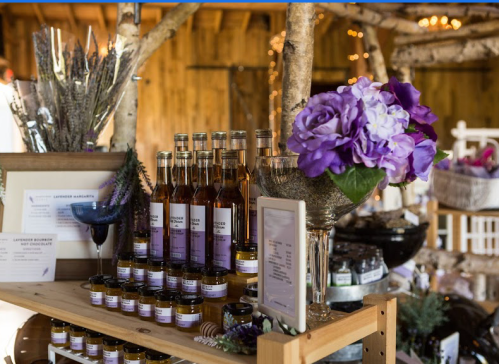 A rustic display of lavender products, including bottles and jars, with purple flowers in a vase and warm lighting.