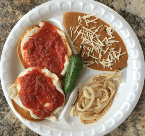 A plate with two eggs topped with red sauce, refried beans with cheese, grilled onions, and a jalapeño pepper.