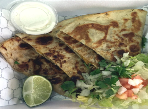 A container with four golden-brown quesadillas, a lime wedge, fresh salad, and a small cup of sauce.