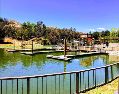 A serene lake with wooden docks, surrounded by greenery and hills under a clear blue sky.