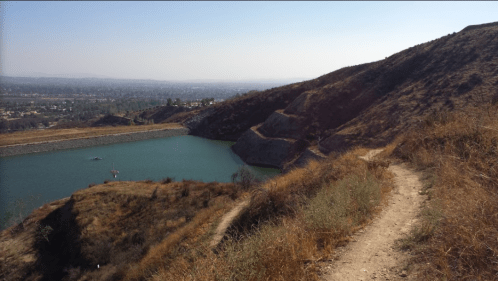 A scenic view of a reservoir surrounded by hills and dry grass under a clear blue sky.