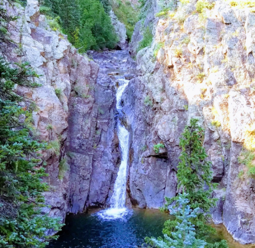 A serene waterfall cascading down rocky cliffs into a clear pool, surrounded by lush green trees.