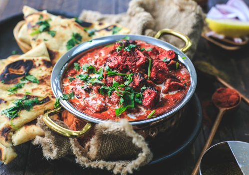 A bowl of creamy red curry topped with cilantro, served with naan bread on a rustic wooden table.