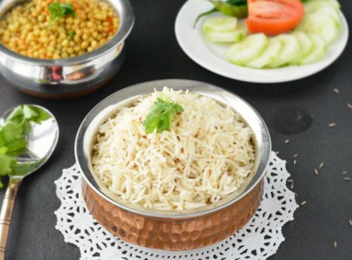 A bowl of fragrant rice garnished with cilantro, alongside lentils and fresh vegetables on a black background.