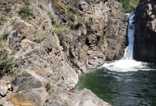 A waterfall cascades into a green pool, surrounded by rocky cliffs and lush vegetation.