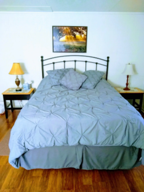 A neatly made bed with gray bedding, two lamps on nightstands, and a framed picture on the wall.