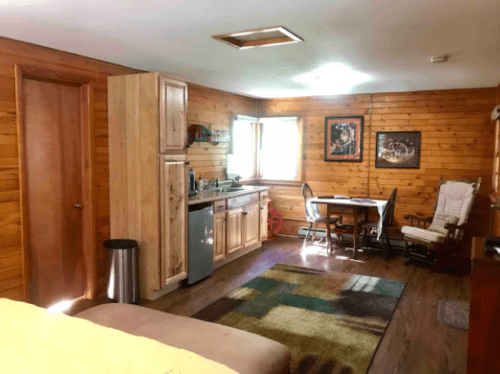 Cozy wooden interior of a small cabin with a kitchenette, dining table, and a rocking chair.