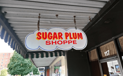 Sign for "Sugar Plum Shoppe" hanging from a storefront awning, with a colorful cloud design.