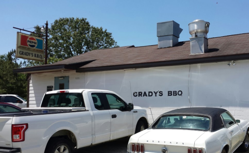 A white pickup truck and a classic car parked outside Grady's BBQ, a small restaurant with a Pepsi sign.