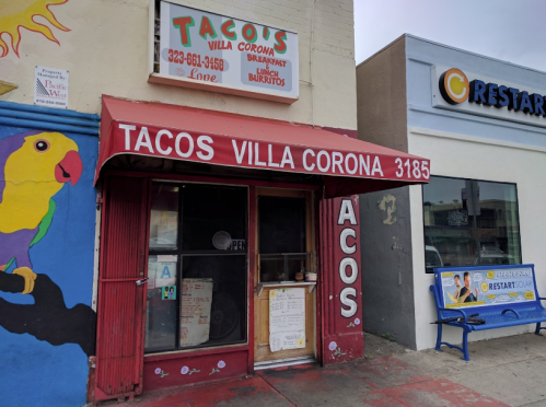 A colorful storefront of Tacos Villa Corona with a red awning and a menu displayed outside.
